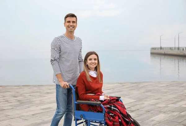 Mujer joven discapacitada en silla de ruedas y su marido cerca del río — Foto de Stock