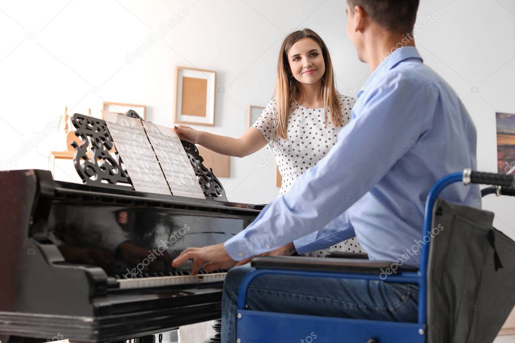 Woman teaching young man in wheelchair to play piano