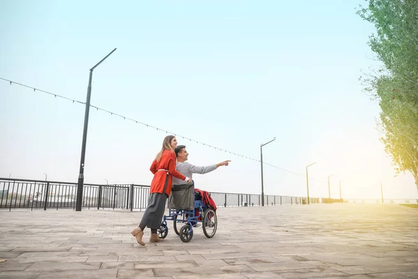 Handicapped young man in wheelchair and his wife outdoors — Stock Photo, Image