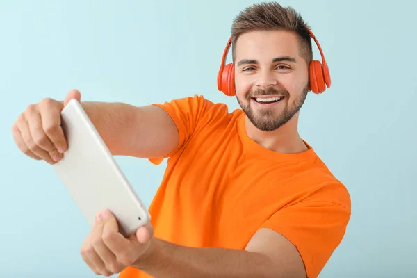 Young man with tablet computer playing video game on color background — 스톡 사진