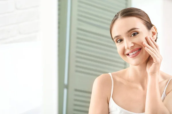 Hermosa joven aplicación de crema facial delante del espejo — Foto de Stock