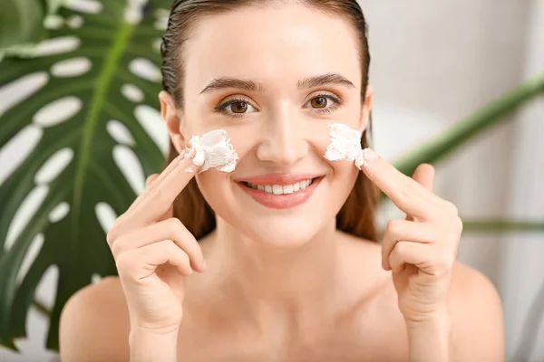 Hermosa joven aplicación de crema facial en casa — Foto de Stock