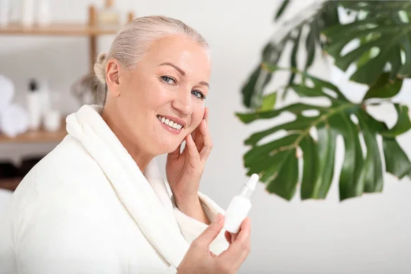 Beautiful mature woman with face serum at home — Stock Photo, Image