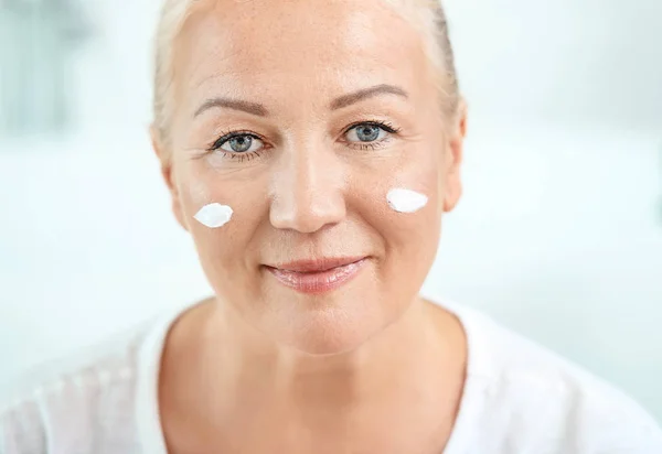 Mulher madura bonita aplicando creme facial em casa — Fotografia de Stock