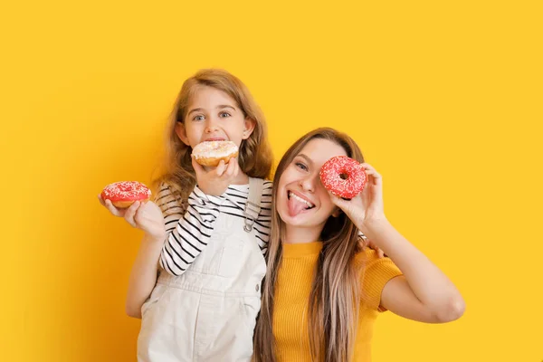 Cute mother and little daughter with tasty donuts on color background — Stock Photo, Image