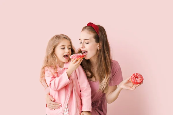 Linda madre e hija pequeña con rosquillas sabrosas en el fondo de color — Foto de Stock