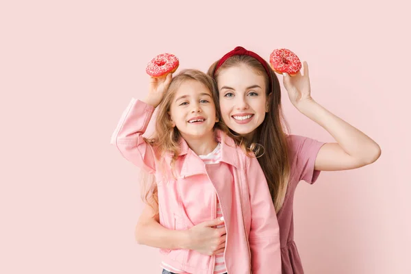 Cute mother and little daughter with tasty donuts on color background — 스톡 사진