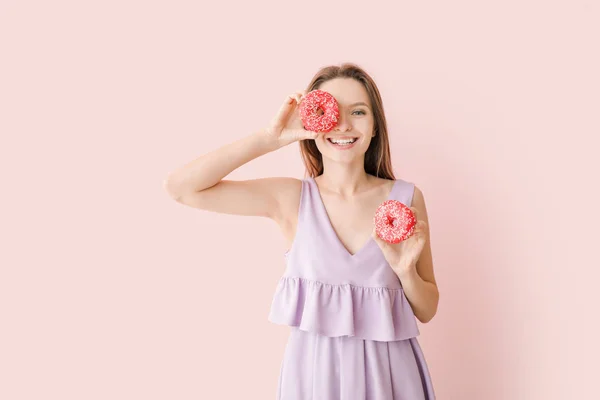 Jeune femme drôle avec des beignets savoureux sur fond de couleur — Photo