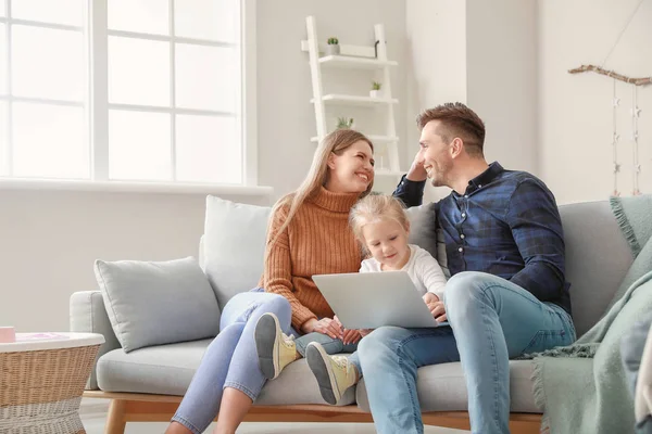 Happy young family with laptop sitting on sofa at home — Stock Photo, Image