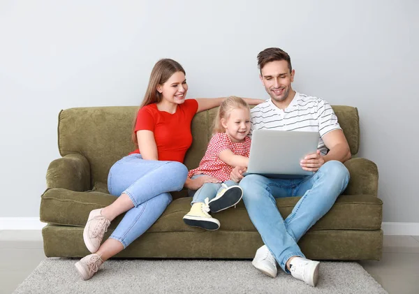 Glückliche junge Familie mit Laptop sitzt auf Sofa in der Nähe von Lichtwand — Stockfoto