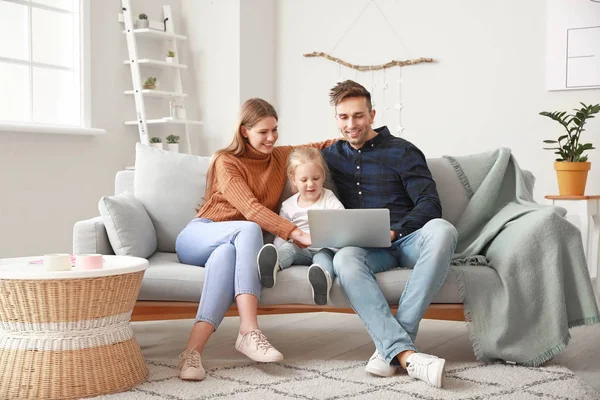 Gelukkig jong gezin met laptop zittend op de bank thuis — Stockfoto