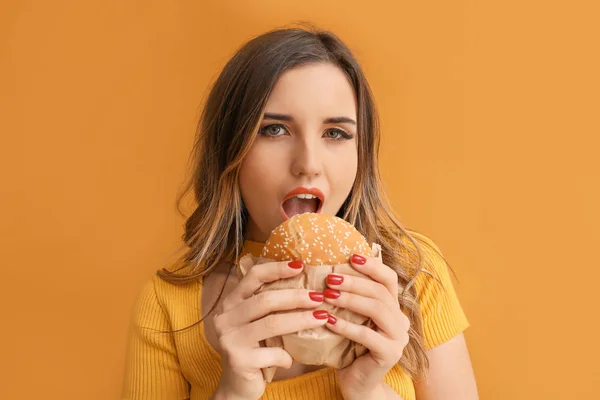 Porträt der schönen jungen Frau mit Burger auf farbigem Hintergrund — Stockfoto