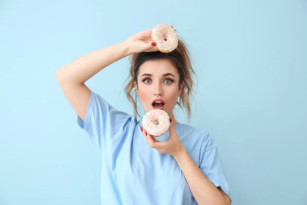 Surprised young woman with donuts on color background — Stock Photo, Image