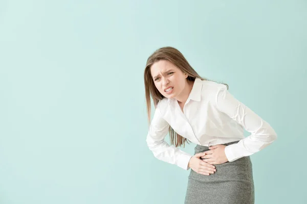 Joven mujer de negocios que sufre de dolor abdominal en el fondo de color — Foto de Stock