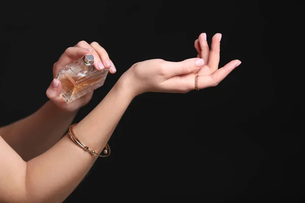 Hands of beautiful young woman with bottle of perfume on dark background — Stock Photo, Image