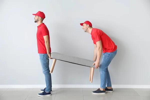 Loaders carrying furniture against light wall — Stock Photo, Image