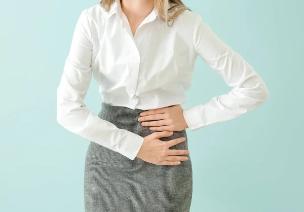 Joven mujer de negocios que sufre de dolor abdominal en el fondo de color — Foto de Stock