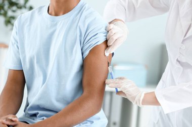 Klinikte genç bir çocuğu aşılayan doktor, yakın plan.