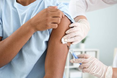 Klinikte genç bir çocuğu aşılayan doktor, yakın plan.
