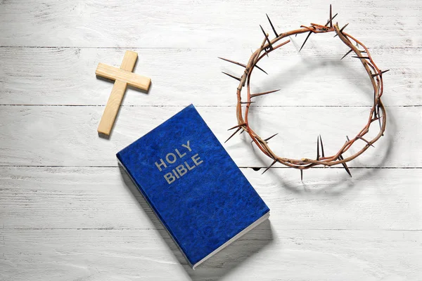 Wreath of thornes, cross and Bible on wooden background