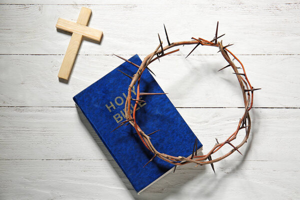 Wreath of thornes, cross and Bible on wooden background