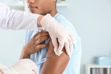 Klinikte genç bir çocuğu aşılayan doktor, yakın plan.