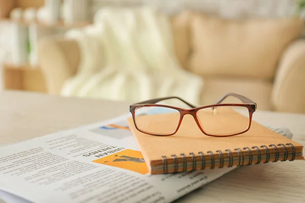 Stylish eyeglasses with newspaper and notebook on table at home