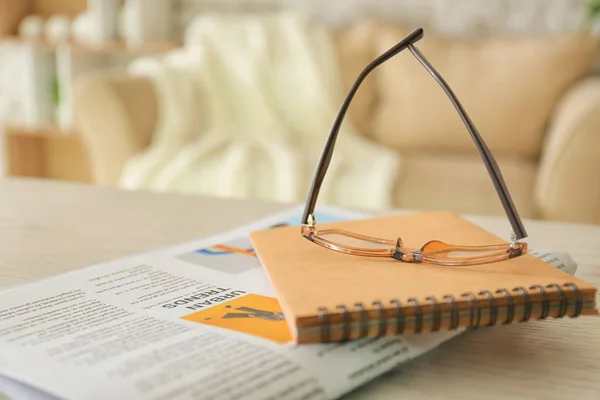 Stylish eyeglasses with newspaper and notebook on table at home