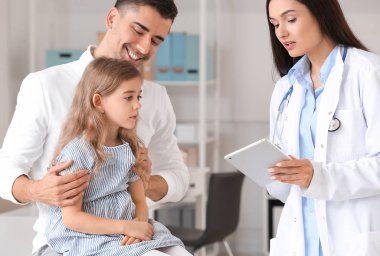 Küçük kızıyla birlikte çocuk doktorunu klinikte ziyaret eden bir adam.