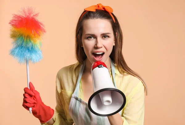 Young housewife with dust brush and megaphone on color background — Stock Photo, Image