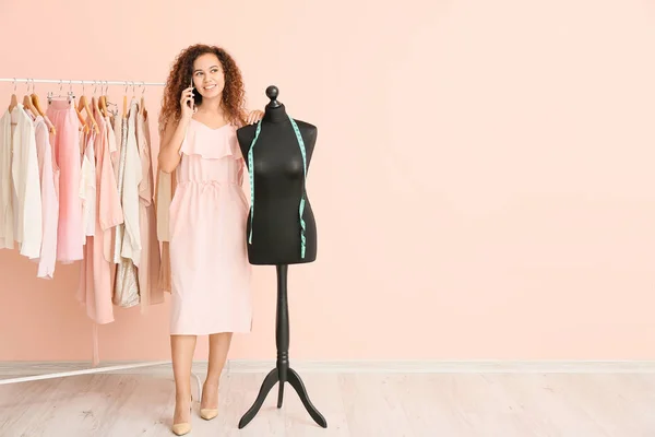 African-American stylist talking by phone near mannequin and rack with modern clothes — Stock Photo, Image