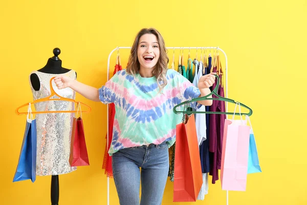 Female stylist with shopping bags near rack with modern clothes