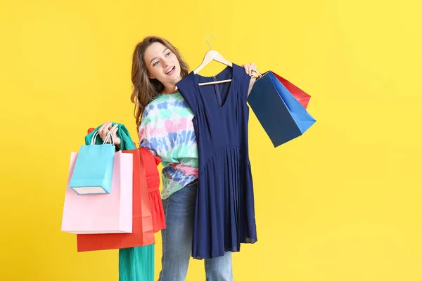 Female stylist with shopping bags on color background