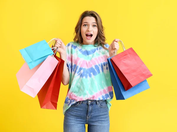 Schockierte Stylistin mit Einkaufstaschen auf farbigem Hintergrund — Stockfoto