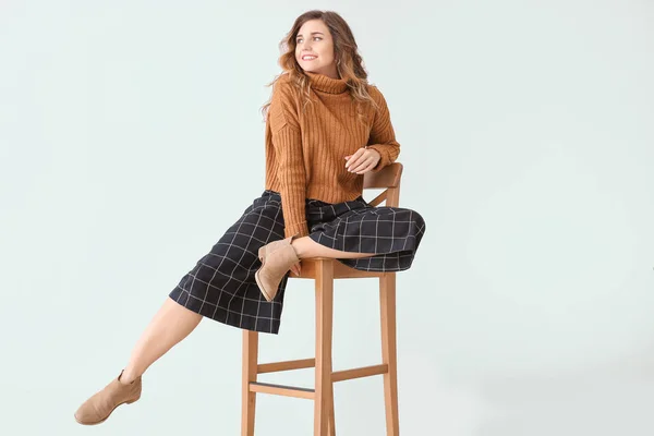 Красивая молодая женщина в теплом свитере сидит на стуле у светлой стены — стоковое фото