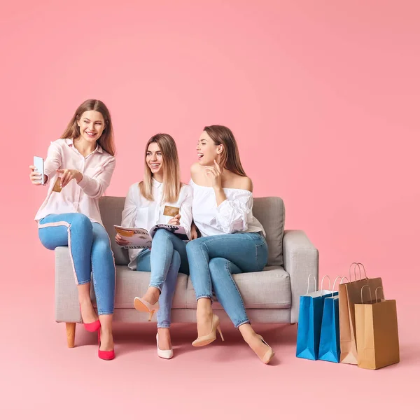 Mujeres jóvenes con bolsas de compras, tarjetas de crédito y teléfono móvil sentado en el sofá contra el fondo de color — Foto de Stock