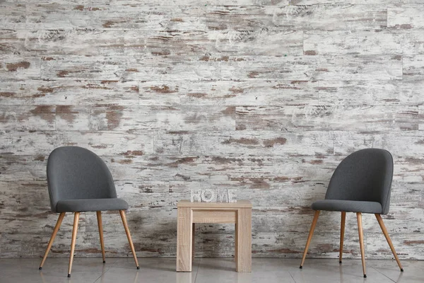 Стильные стулья со столом рядом с деревянной стеной в номере — стоковое фото