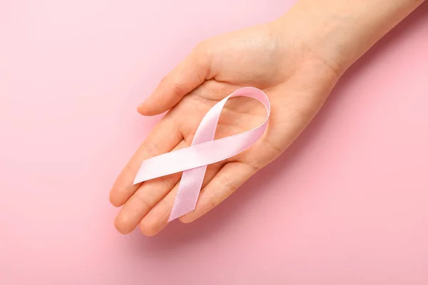 Female hand with pink ribbon on color background. Cancer awareness concept — Stock Photo, Image