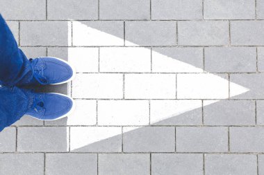 Young man standing on road with arrow marking, top view. Concept of choice