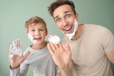 Komik bir baba ve oğlu, renkli arka plana karşı yüzlerine tıraş köpüğü sürüyor.