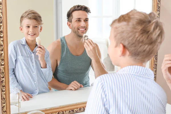 Father with son applying shaving foam onto their faces in bathroom