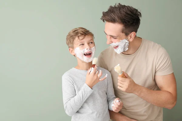 Πατέρας με γιο εφαρμογή αφρού ξυρίσματος στα πρόσωπά τους με φόντο το χρώμα — Φωτογραφία Αρχείου