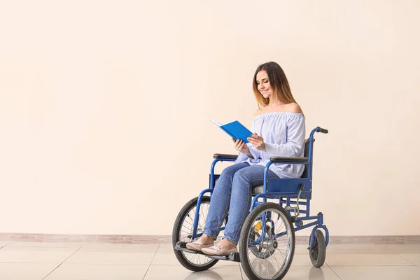 Mujer joven discapacitada en silla de ruedas y con libro cerca de la pared de color — Foto de Stock