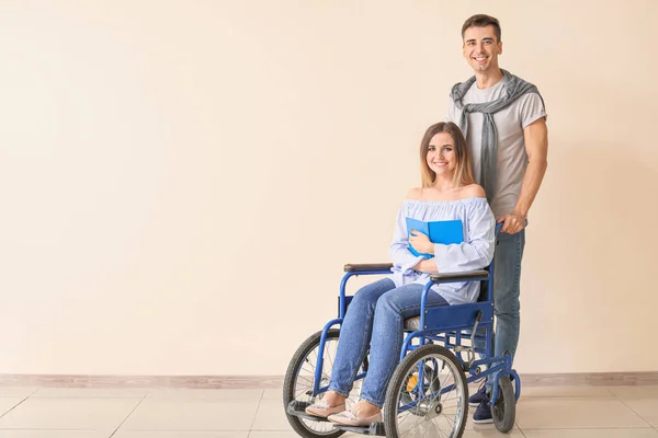 Handicapped young woman with book and her husband near color wall — Stock Photo, Image