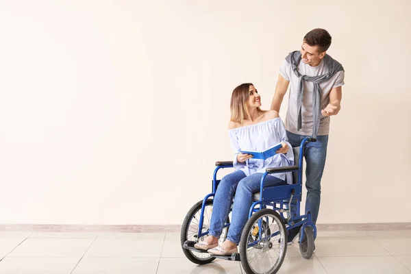 Handicapped young woman with book and her husband near color wall — Stock Photo, Image