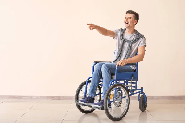 Handicapped young man in wheelchair pointing at something near color wall — 图库照片