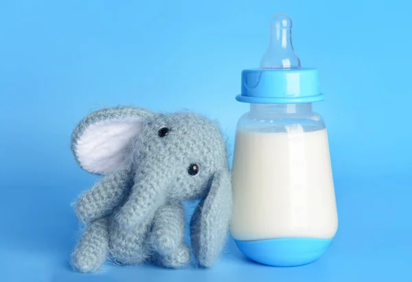 Bottle of milk for baby and toy on color background