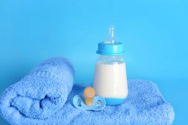 Bottle of milk for baby, towel and pacifier on color background