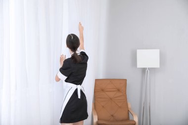 Otel odasında perdeleri açan güzel oda hizmetçisi.