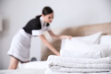 Otel odasında yatak yapan güzel oda hizmetçisi, havlulara odaklan.
